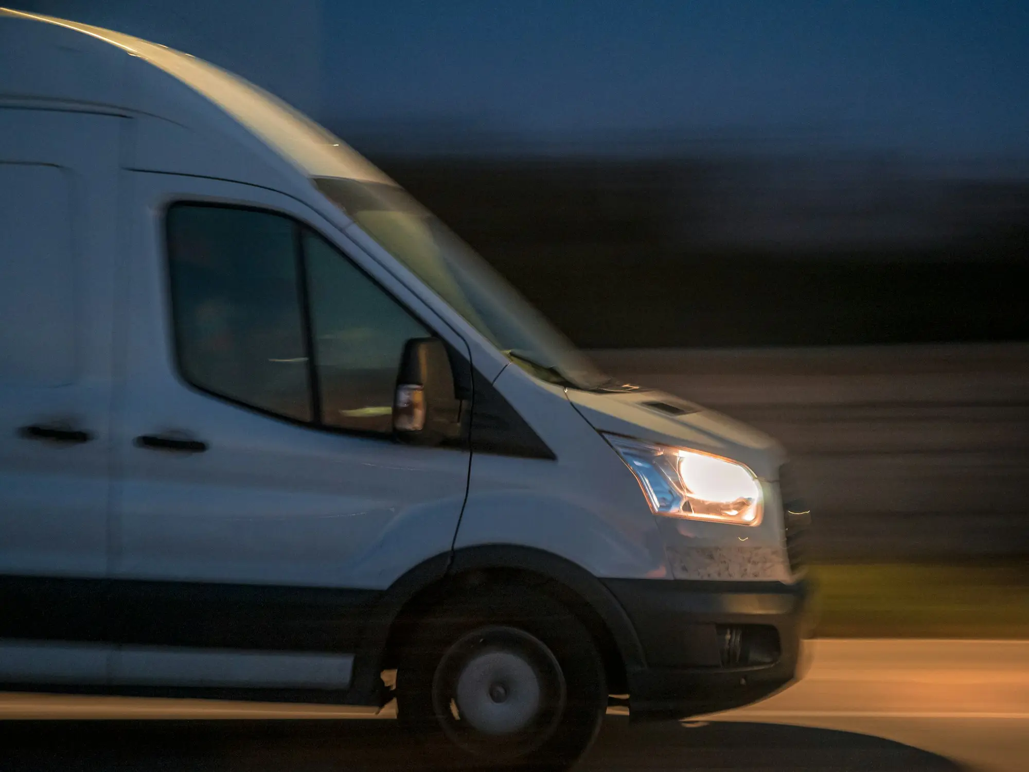 White courier van driving down a street at night